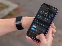Eine Person hält ein Smartphone, das die Whoop-App zeigt, mit einem Fitness-Tracker am Handgelenk.