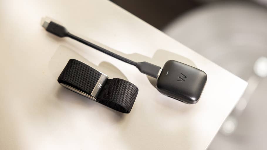 Ein schwarzes tragbares Gerät mit einem Armband und einem Ladekabel auf einer weißen Fläche.