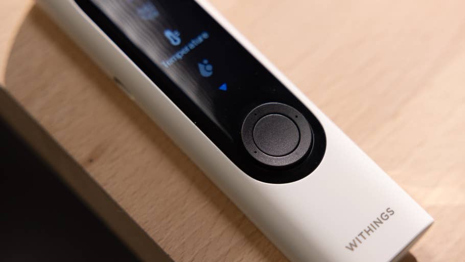 Ein Withings BeamO-Thermometer auf einer Holzoberfläche, das eine Anzeige mit Temperaturanzeige zeigt.