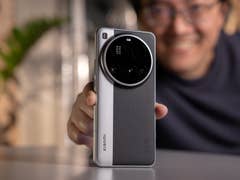 Eine Person hält ein Xiaomi 15 Ultra-Smartphone und lächelt mit grünem Hintergrund.