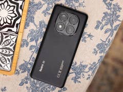 Schwarzes Xiaomi Redmi Note 14 Pro 5G-Smartphone auf einem blumengemusterten Tischläufer.