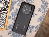 Schwarzes Xiaomi Redmi Note 14 Pro 5G-Smartphone auf einem blumengemusterten Tischläufer.