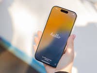 Eine Hand hält ein Apple iPhone 16 Pro, das einen bunten 'hallo' Bildschirm zeigt.