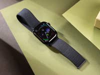 Eine schwarze Apple Watch Series 10 auf grünen und braunen Flächen, die verschiedene Apps anzeigt.