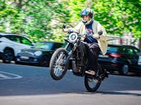 Eine Person, die auf einem Motorrad einen Wheelie auf einer Straße mit geparkten Autos macht.