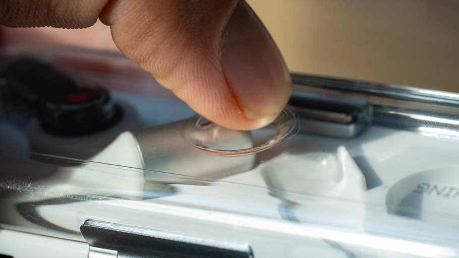 Ein Finger drückt einen transparenten Knopf auf einer Hülle, die Nothing Ear Kopfhörer enthält.