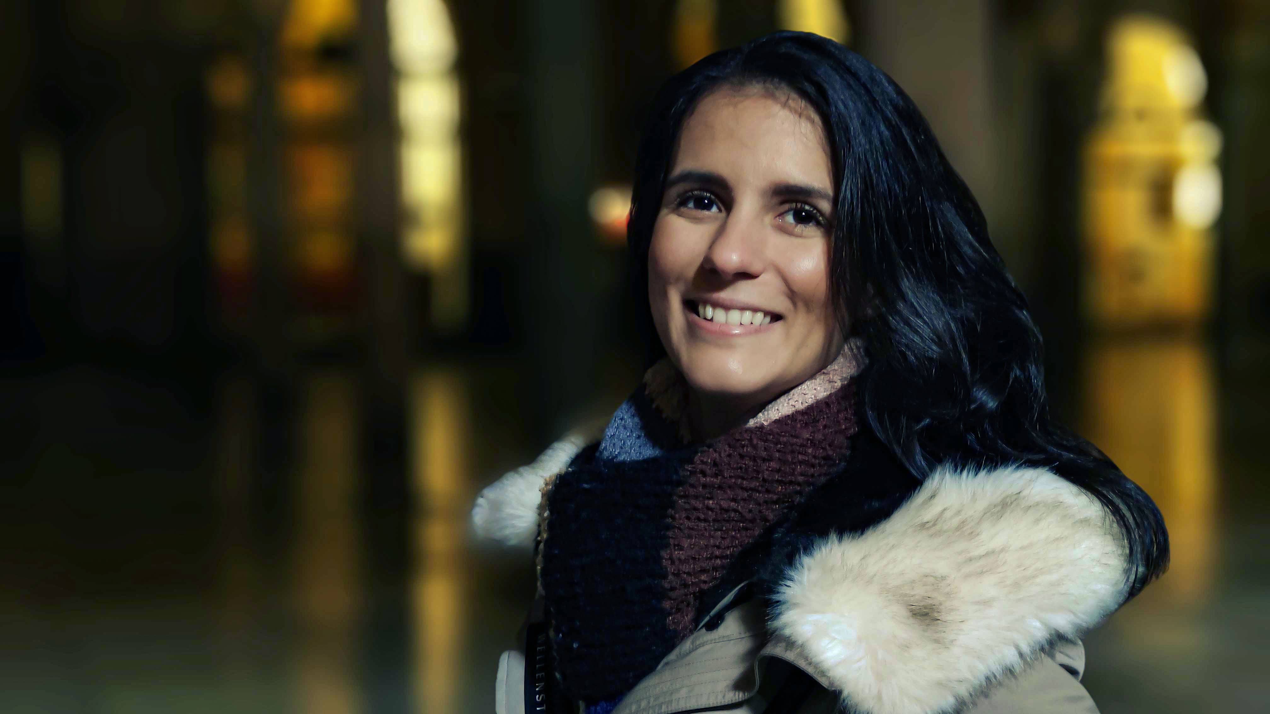 Eine lächelnde Frau in der Nachtfotografie, mit sanfter Beleuchtung und verschwommenem Hintergrund.