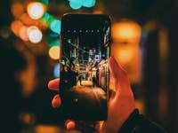 Eine Hand hält ein Smartphone, das eine hell erleuchtete Gasse zeigt.