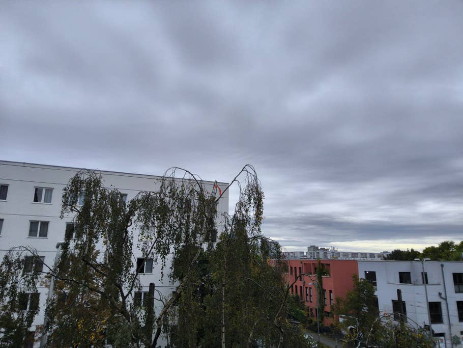 Eine Sicht auf einen bewölkten Himmel über Gebäuden mit Bäumen im Vordergrund.