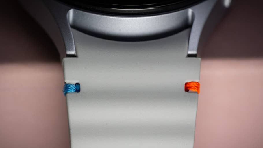 Nahaufnahme einer Samsung Galaxy Watch 7 mit grauem Armband und blauen und orangefarbenen Akzenten.