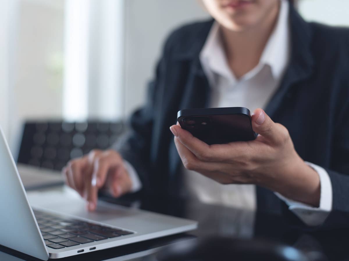 Eine Frau sitzt am Laptop und schaut auf ihr Handy