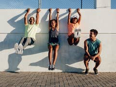 Vier Personen, die an einer Wand trainieren, lächeln und sind in Fitnessaktivitäten engagiert.