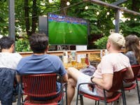 Gruppe von Freunden, die ein Fußballspiel auf einem Sylvox 4K Fernseher im Garten ansehen.