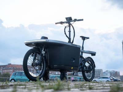 Ein Terran T1 Pro E-Lastenrad, das neben einer Treppe mit einer Stadtsilhouette im Hintergrund geparkt ist.