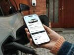 Ein E-Auto wird geladen, ein Handy zeigt den Strompreis an