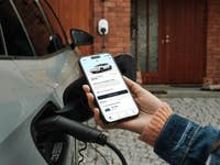 Ein E-Auto wird geladen, ein Handy zeigt den Strompreis an
