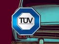 TÜV Logo vor einem alten Auto.