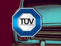 TÜV Logo vor einem alten Auto.