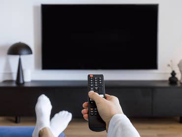 Eine Person hält eine Fernbedienung vor einem schwarzen Smart-TV.