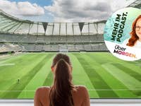 Eine Frau, die in ihrem Wohnzimmer auf einen riesigen Fernseher schaut, wo ein Fußballstadion von innen zu sehen ist