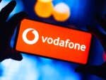 Eine Hand hält ein Smartphone mit dem Vodafone-Logo auf rotem Hintergrund.