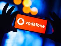 Eine Hand hält ein Smartphone mit dem Vodafone-Logo auf rotem Hintergrund.
