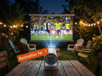 Ein Beamer wirft ein Fußballspiel zwischen Deutschland und Brasilien an eine Leinwand in einem Garten bei Nacht.