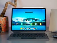 Ein Xiaomi Pad 7 auf einem Tisch mit einer Tastatur, einer Kamera und einer Blume im Hintergrund.