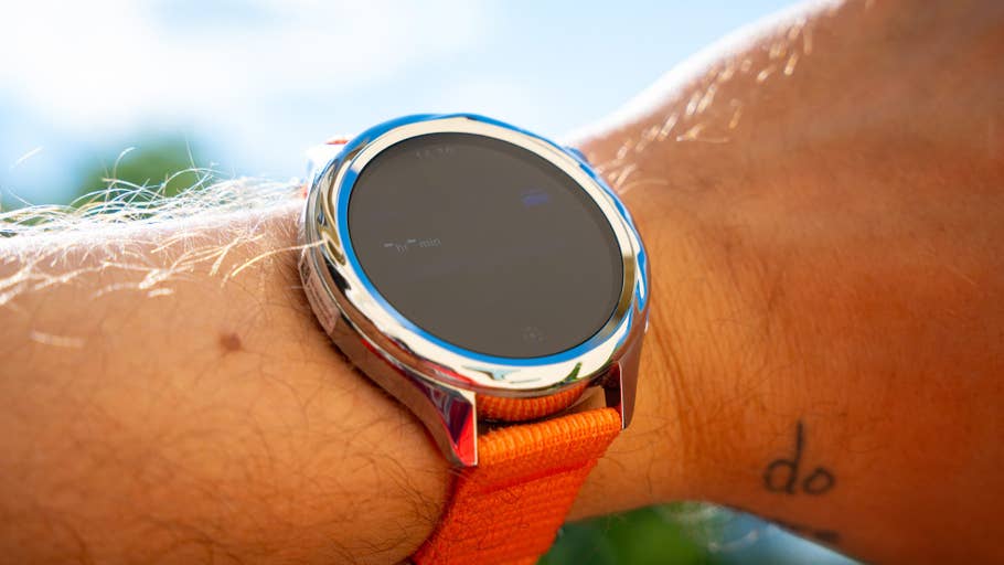 Eine Xiaomi Watch S4 auf einem Handgelenk mit orangefarbenem Armband, das einen dunklen Bildschirm zeigt.