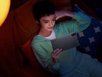 Eine Person, die sich auf einem Sofa entspannt und ein Xiaomi Redmi Pad 2 Tablet in einem schwach beleuchteten Raum verwendet.