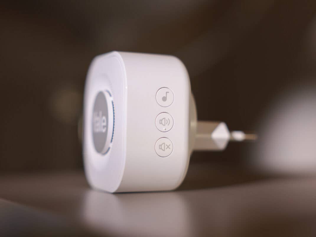 Ein weißer, quadratischer Yale Doorbell Chime mit seitlichen Tasten für Melodie und Lautstärke liegt auf einer Holzoberfläche.